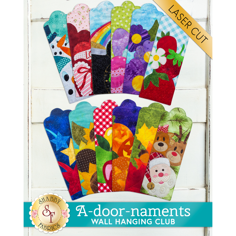 All 12 A-door-nament designs spread out on a white wood background with a gold laser cut banner in the top right.