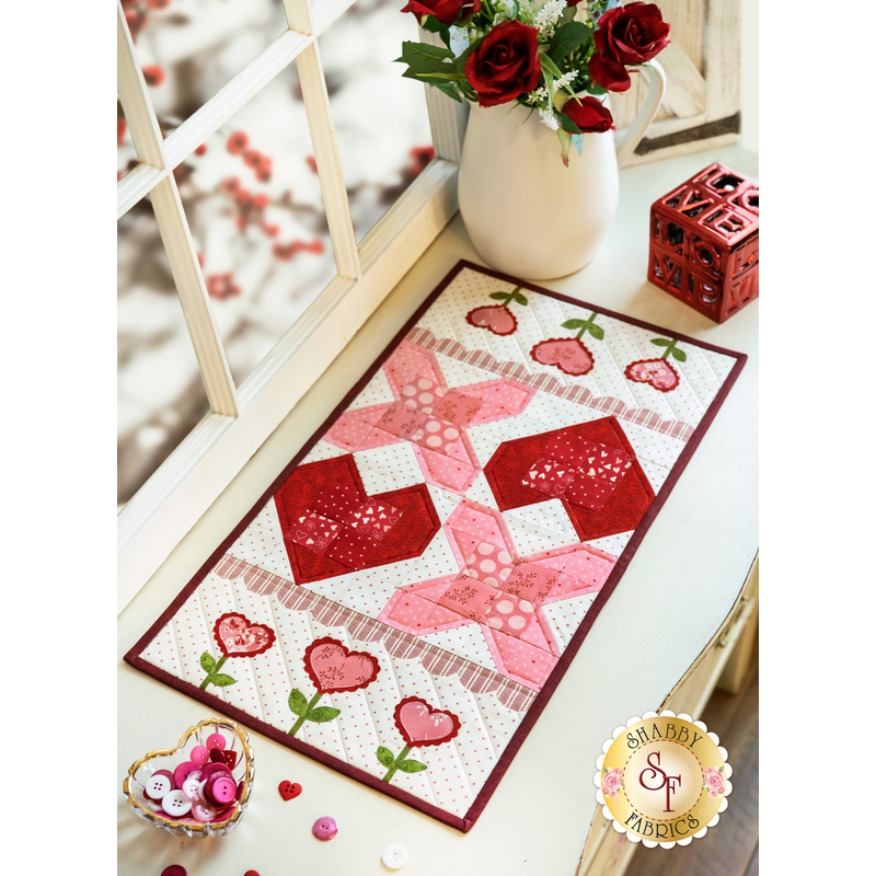 An adorable X's and Hearts table runner with small flowers laid flat on a window sill