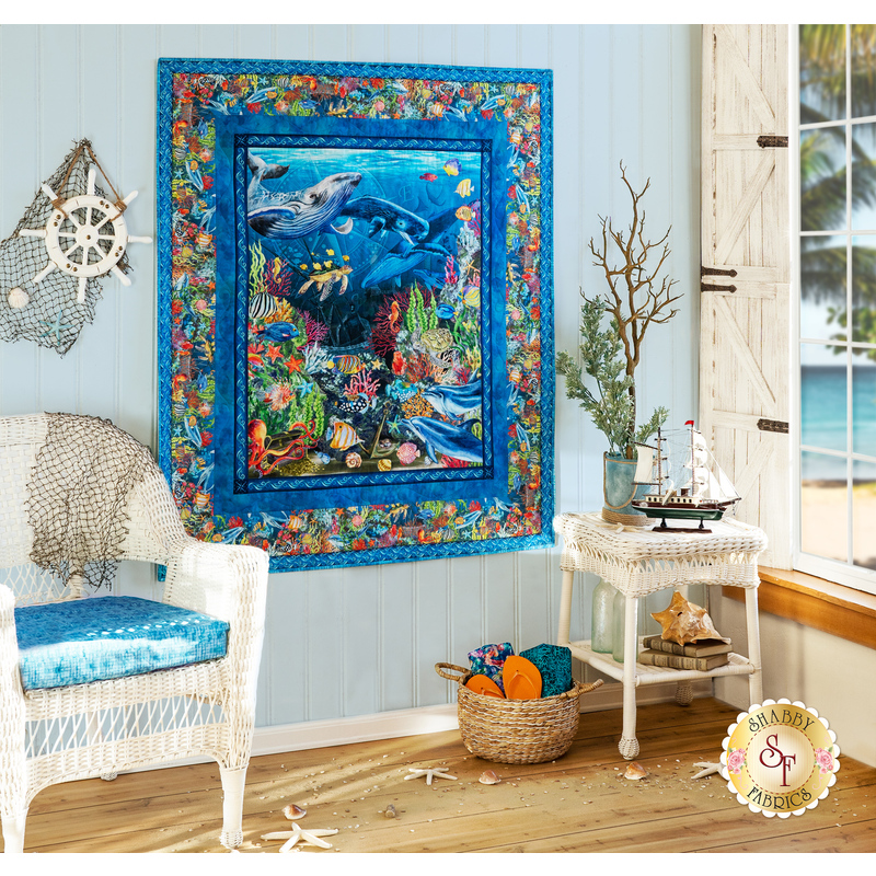 Blue panel quilt featuring many different sea animals including whales, turtles, fish, coral and more hanging on light blue panel wall.