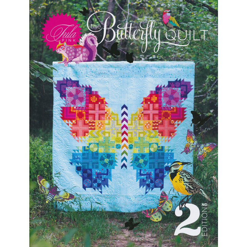 large multi colored butterfly image on a quilt displayed in front of trees and other foliage