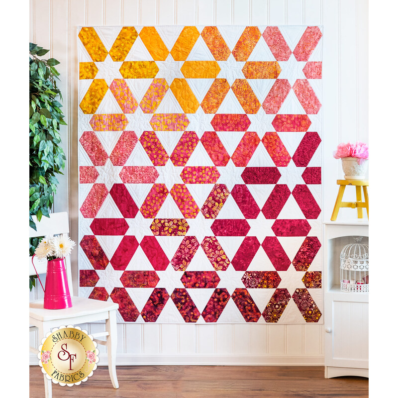 White quilt featuring a multicolor star design pattern hanging on white wood panel wall.