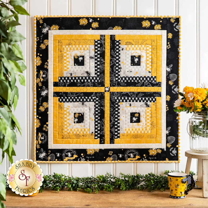 Wall hanging with four blocks made of strips of bee themed and floral fabrics in white, black, and yellow.
