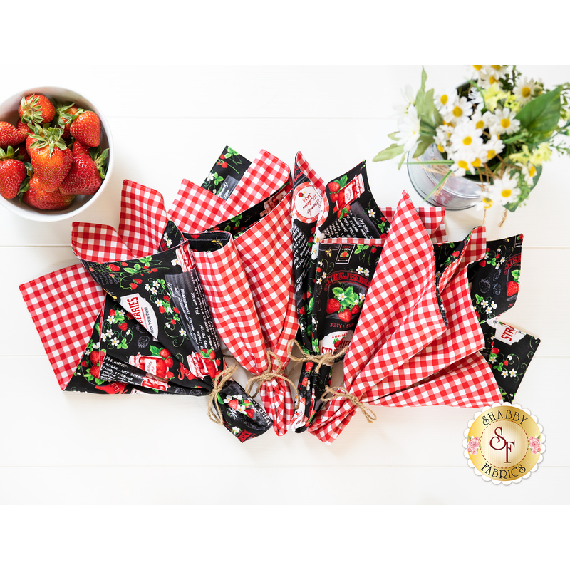 Top down image of cloth napkins arranged in a fan with a bowl of strawberries and vase of daisies nearby