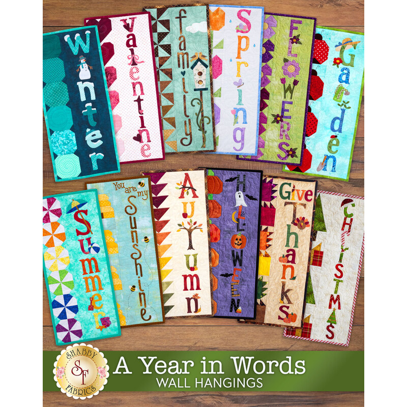 A collage of all 12 A Year In Words Wall Hangings laid flat on a wood table