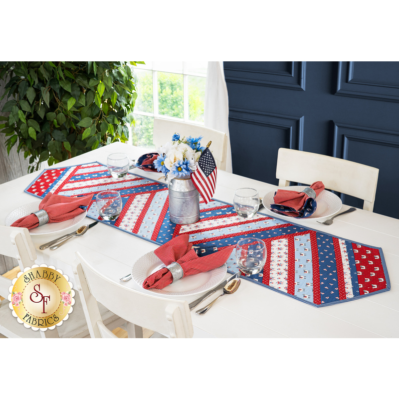 Table runner made of strips of alternating diagonal fabrics in red, white, and blue featuring patriotic motifs.