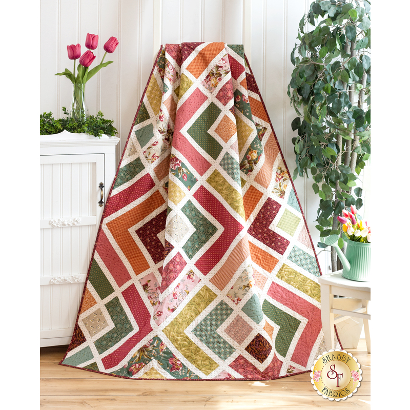 Image of quilt gathered and draped in front of a white cabinet with pink tulips