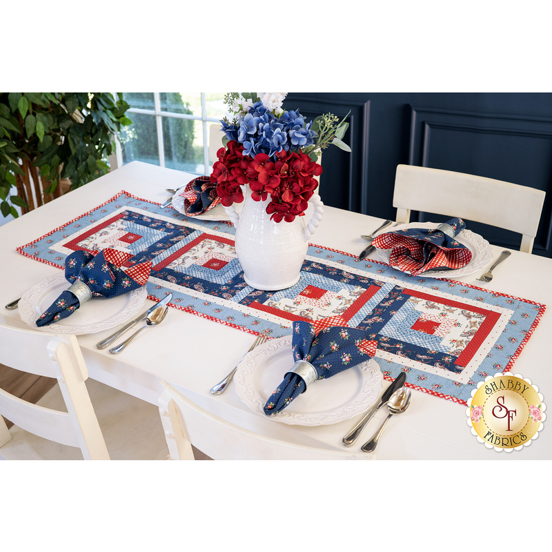 Table runner with square designs made with strips of red, white, and blue fabric featuring floral, paisley, and gingham prints.