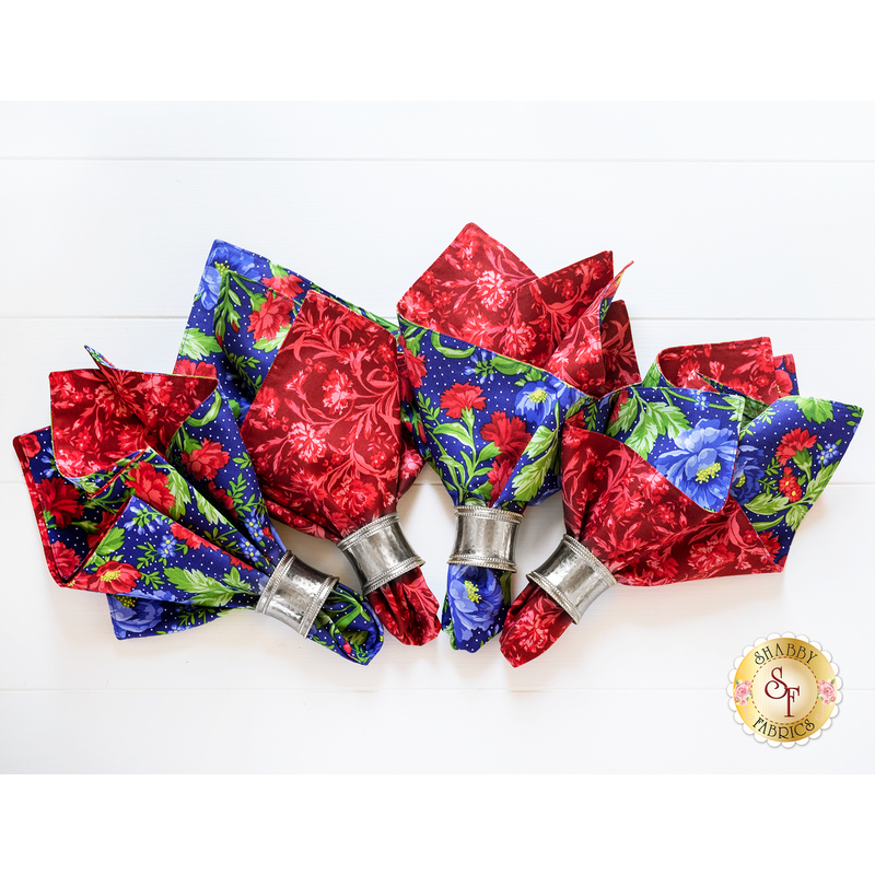 4 cloth napkins made of red and blue floral prints with silver napkin holders on a white background