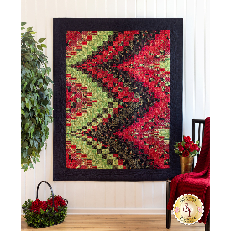 Vibrant quilt with a zigzag pattern in red, green, and black, displayed against a white wall.