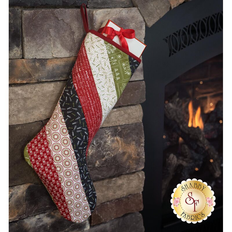 A patchwork Christmas stocking hangs from a stone fireplace next to a glowing fire.