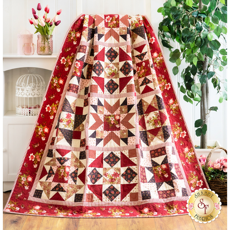 Quilt with geometric piecing made of red, pink, and cream floral fabrics draped over furniture.