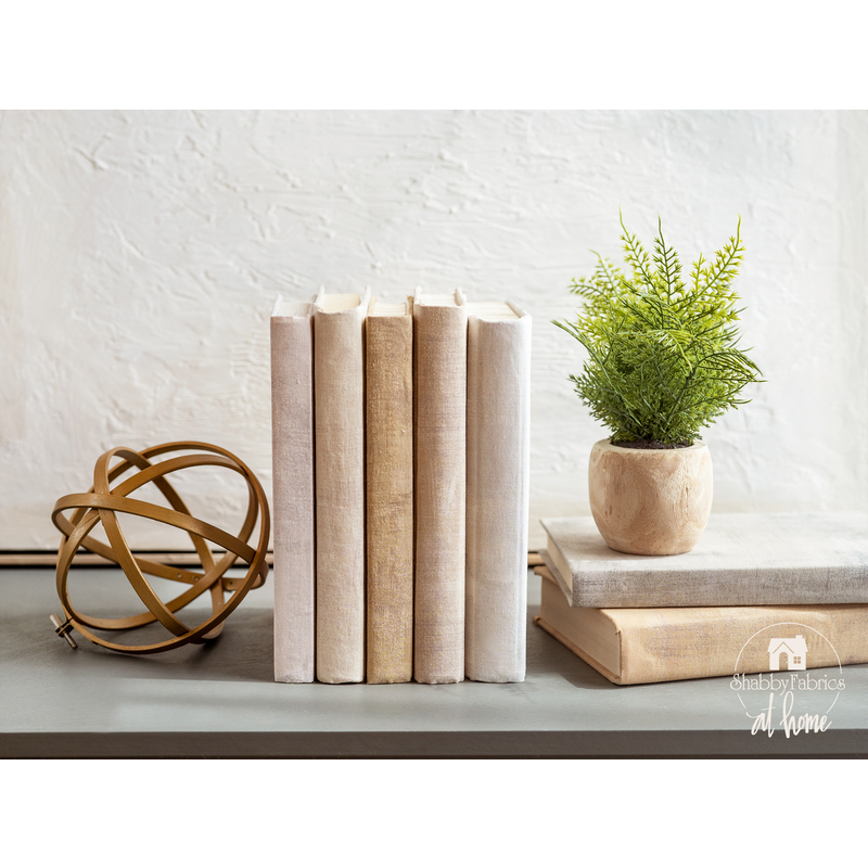 A collection of books with fabric book covers standing on a shelf next to a small plant and home decor