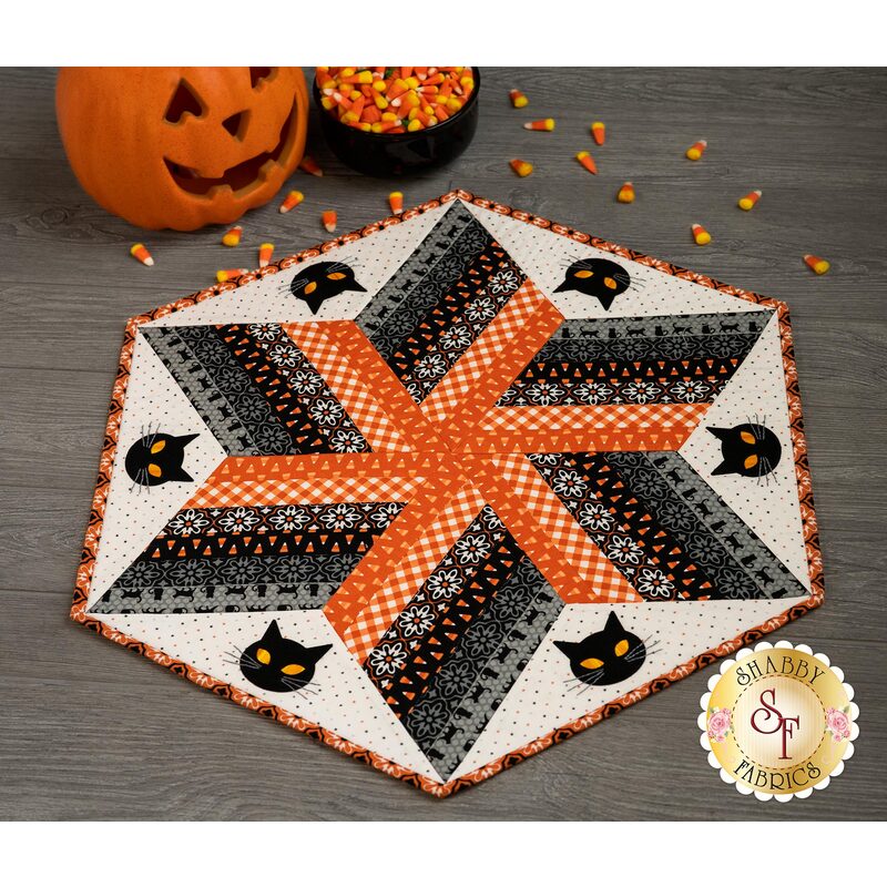 Halloween themed table topper with diamonds made of strips of black and orange fabric on a white background with black cat face appliqué.