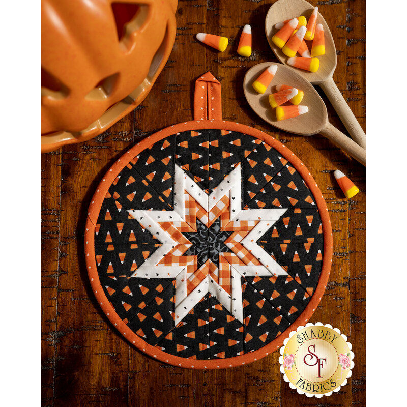 Round hot pad made of black fabric with candy corn print along with orange and white accent fabrics.