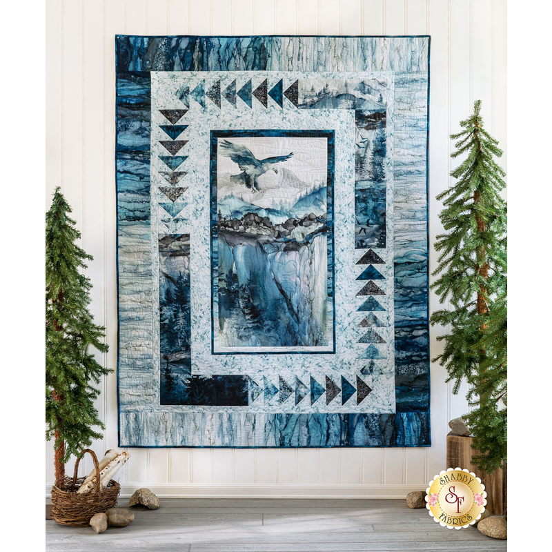 A styled image of the Take Flight Quilt on a white wall surrounded by trees.