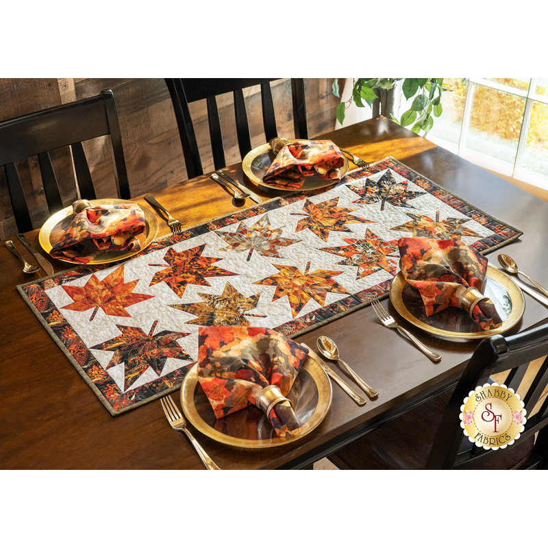 Table runner with two rows of maple leaves made of autumn themed prints on cream background.