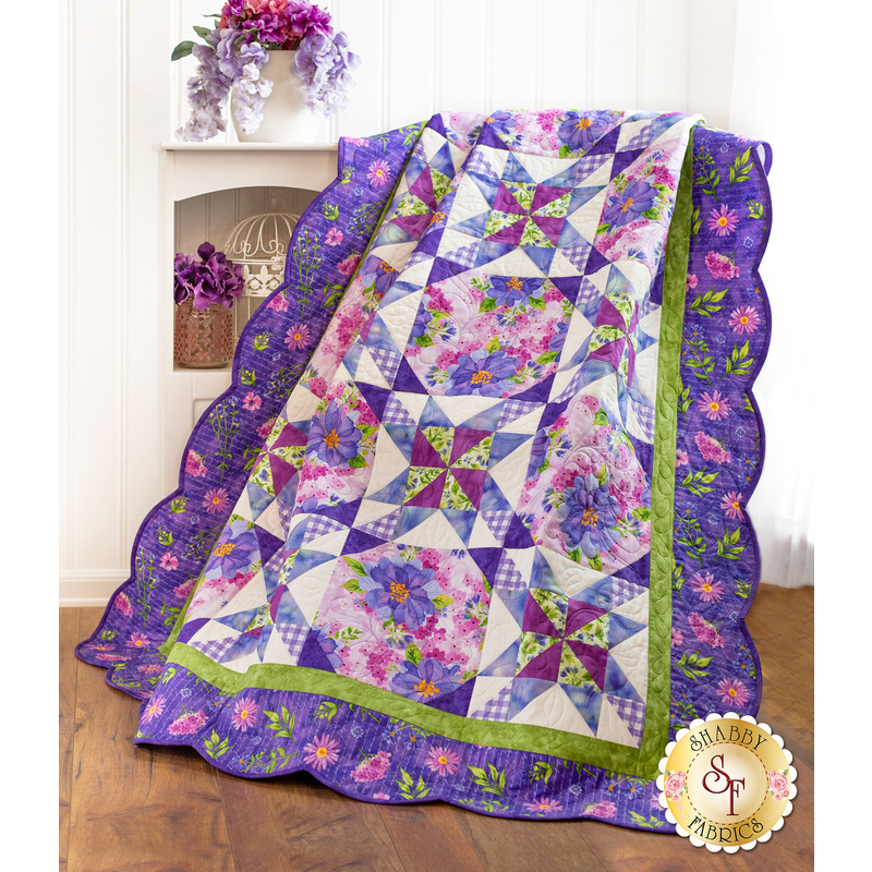 Finished quilt draped over a chair with white walls and vases with purple flowers in the background