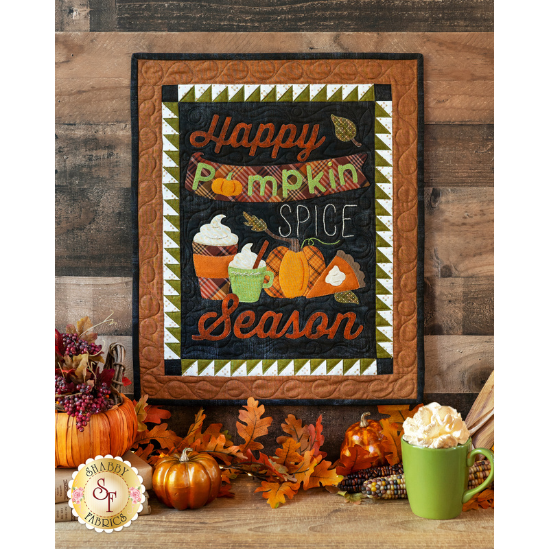 An autumn themed wall hanging with cups of cocoa, leaves, and pumpkins on a wooden wall