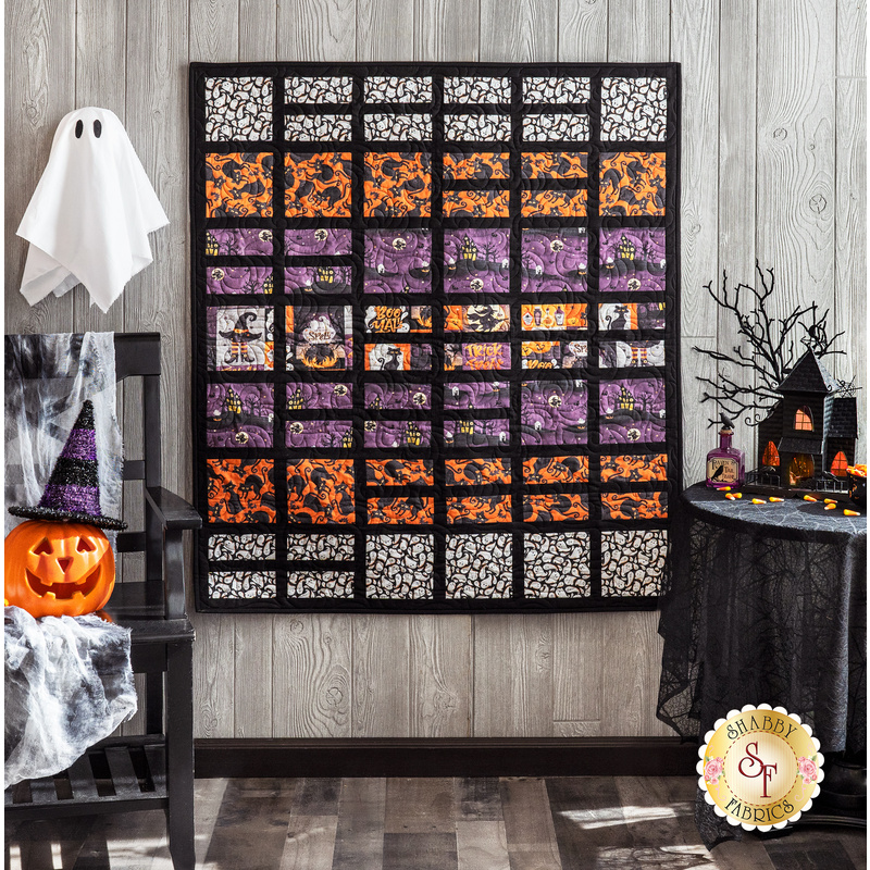A fun blocked Halloween quilt with white, orange, and purple fabrics hung on a wood textured wall