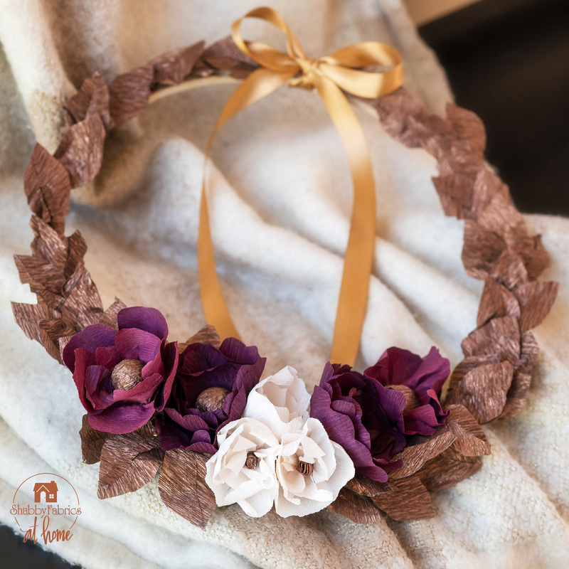 Wreath of foliage and flowers toped with a gold ribbon resting on a towel.