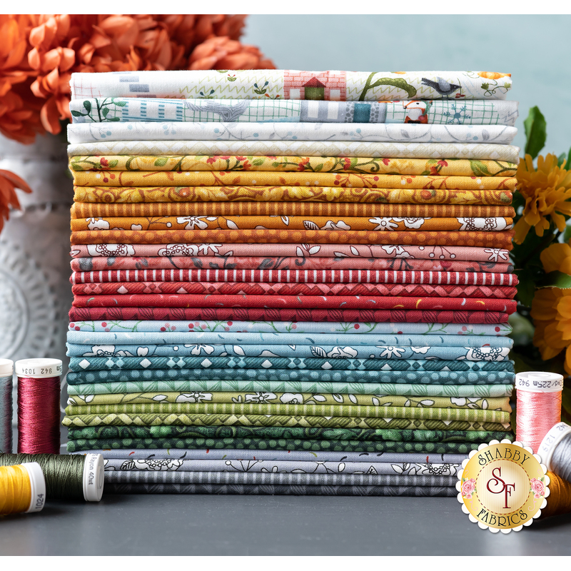 Photo of a stack of fabrics from the Wander Lane II collection with coordinating thread spools and flowers in the background.