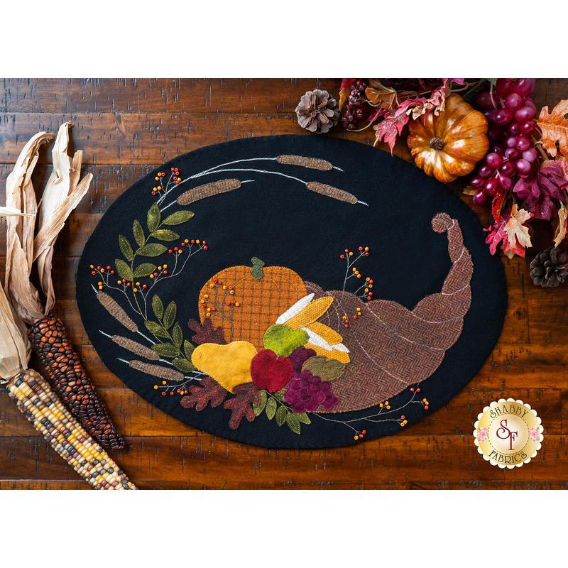 Wool placemat with appliqué of a horn filled with fruits and a pumpkin.