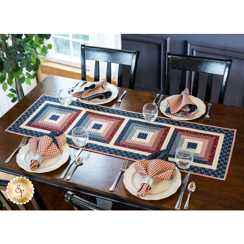 Table runner with four blocks of rectangular strips of fabric, featuring cream, read, and blue patriotic prints.