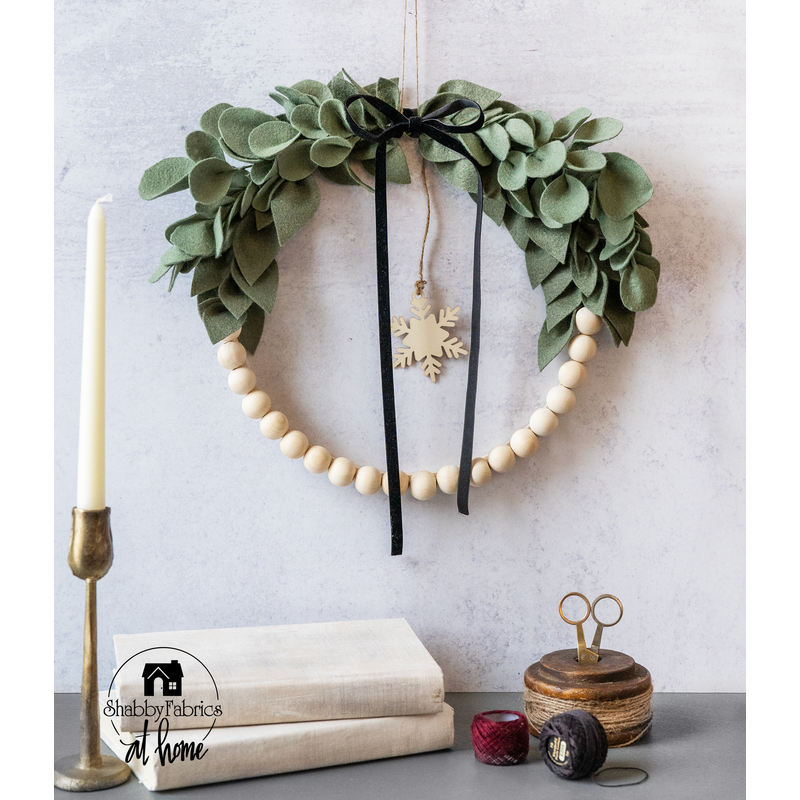 A lightly textured white wall with a minimalist hoop wreath hanging above a counter space with books, a candlestick, and twine with a small pair of scissors.