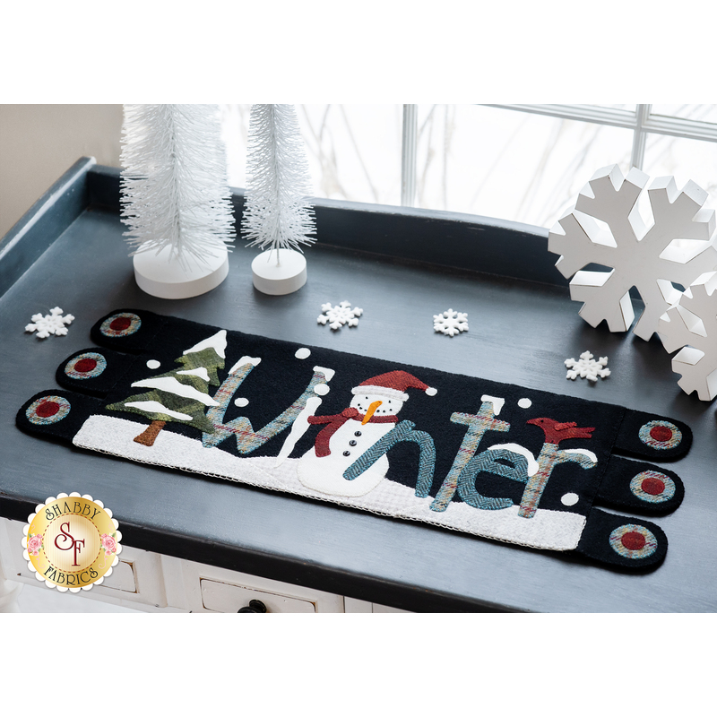 top down image of winter table runner on a tabletop decorated with winter decor items