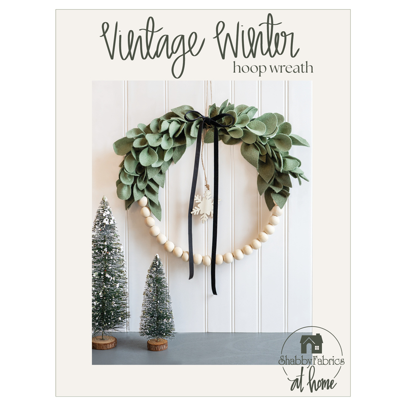 front cover of hoop wreath pattern booklet showing a completed project and evergreen tree decor against a white paneled wall above a dark countertop