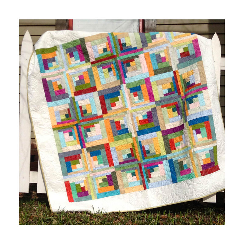 Image of completed geometric quilt draped over a white picket fence in front of a house