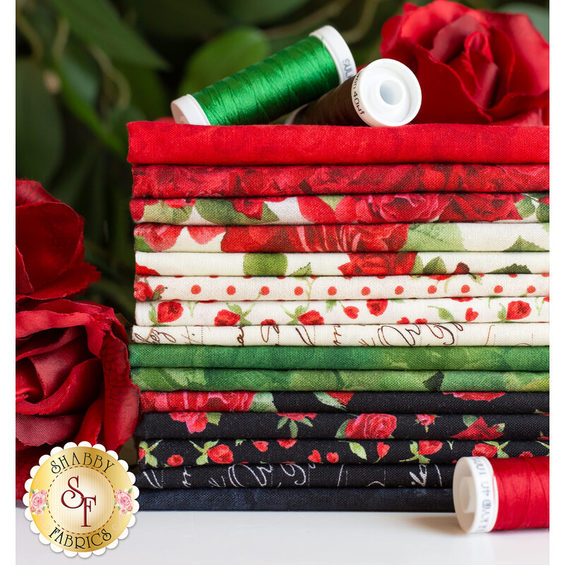 Stack of fabrics in the Vintage Rose collection in white, red, and green, on a white countertop with red roses in the background and spools of thread on the counter and on top of the fabric stack