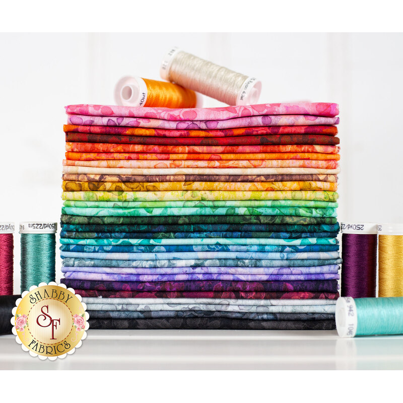 A stack of fabric in a rainbow of colors, surrounded by spools of thread.