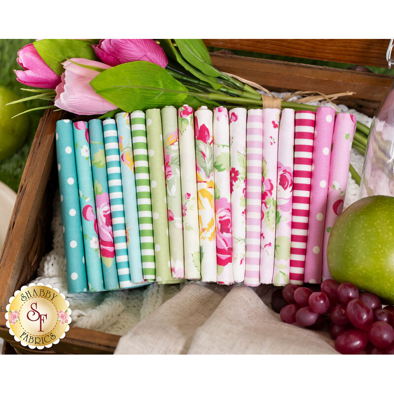 fabrics in the picnic collection, from pinks to blues to greens to creams, folded and stacked inside a picnic basket with flowers and fruit