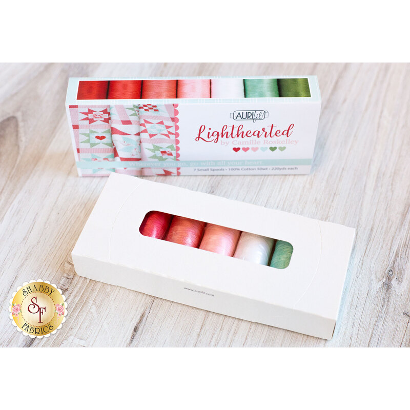 Image of a thread set with red, white, pink, blue, and green spools inside a white box laying on a wooden countertop