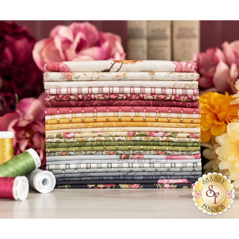 Red, yellow, green and grey floral fabrics stacked and surrounded by flowers, books, and thread.