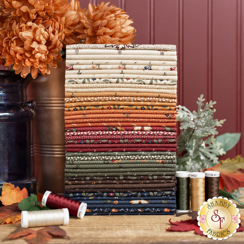 Stack of 40 fat quarters, beautifull staged against an autumnal scene of pale orange flowers and sage. Matching thread spools are scattered about them.
