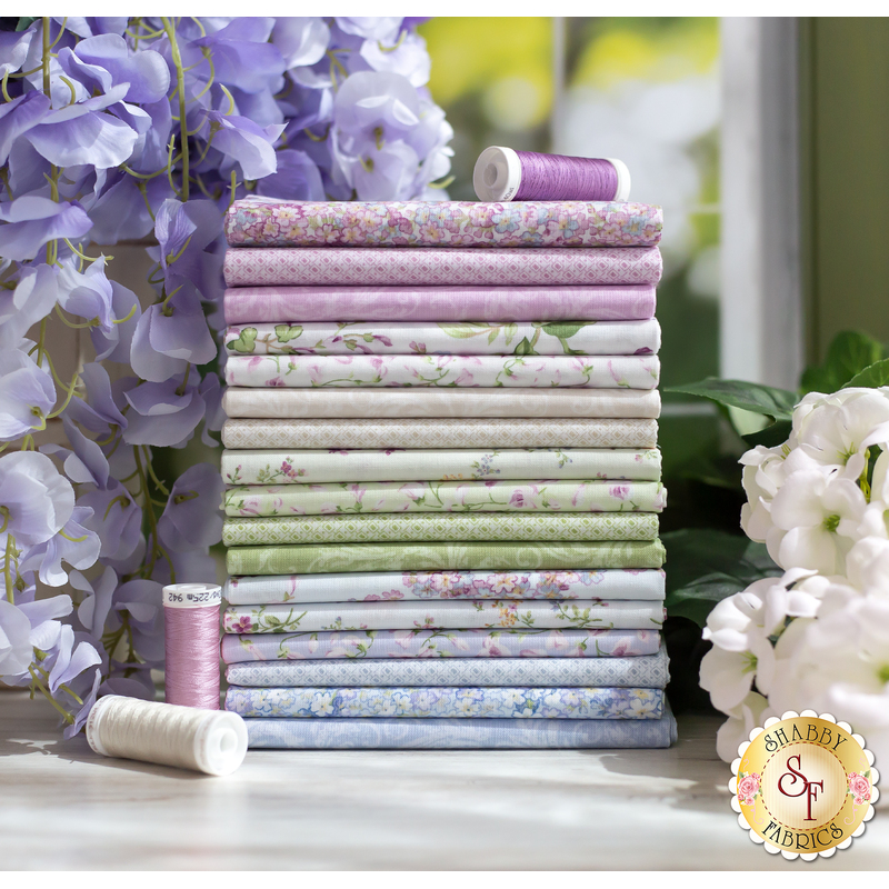 Stack of folded fabrics included in the Sugar Lilac FQ set with coordinating threads and flowers on display.