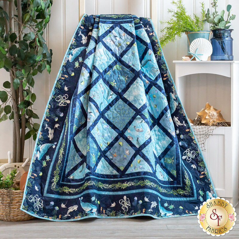 A textured blue quilt draped over a chair, featuring a diamond pattern and ocean-themed motifs.