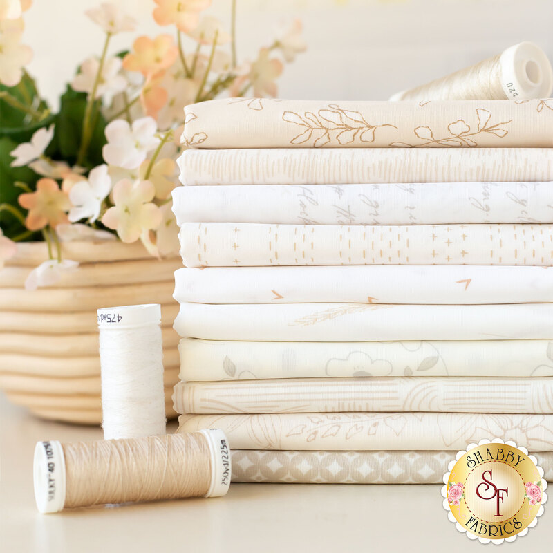 Photo of a stack of 10 neutral pale fabrics with thread spools and flowers in the background.