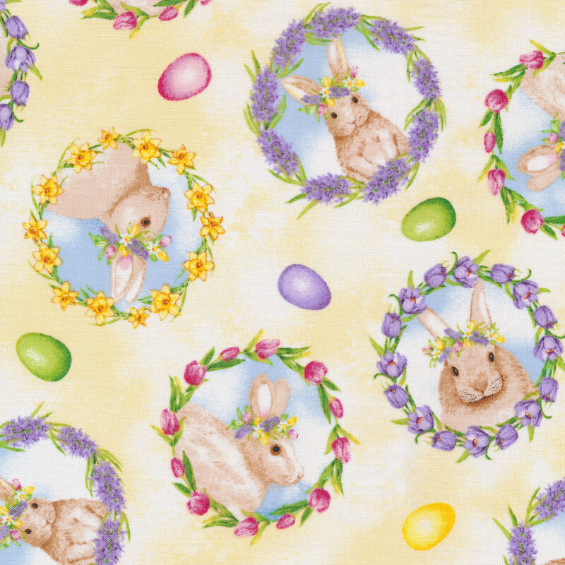 This fabric features bunny motifs in wreaths with tossed colorful eggs on a mottled yellow background