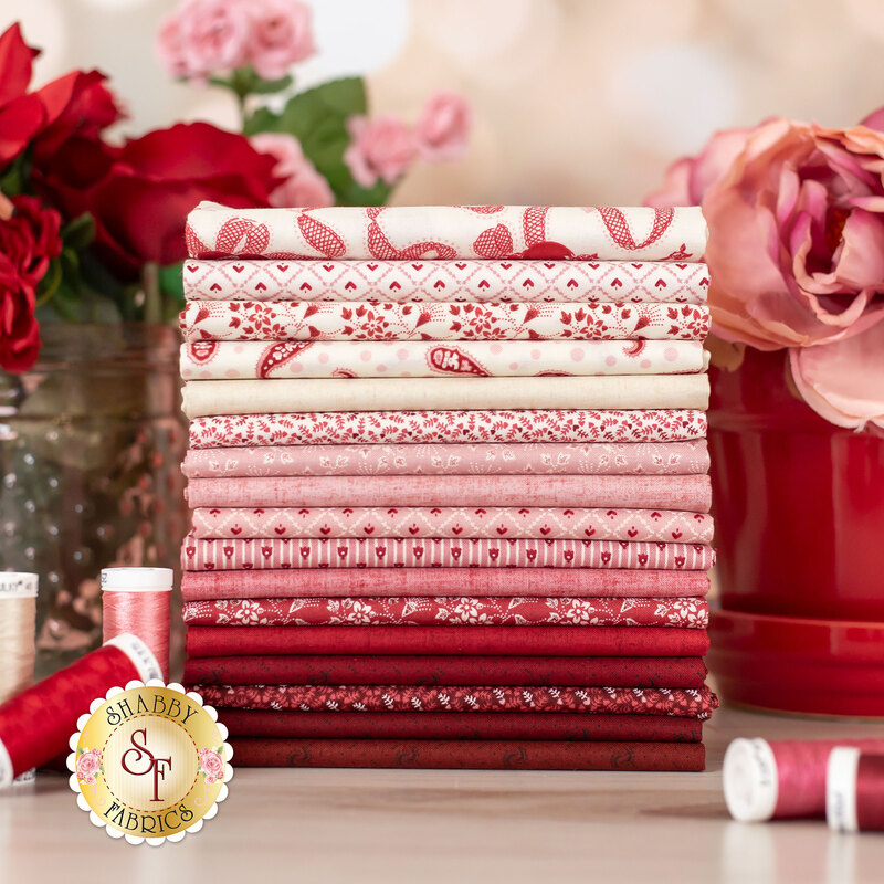 cream, pink, and red fabrics stacked on a wood stable surrounded by roses
