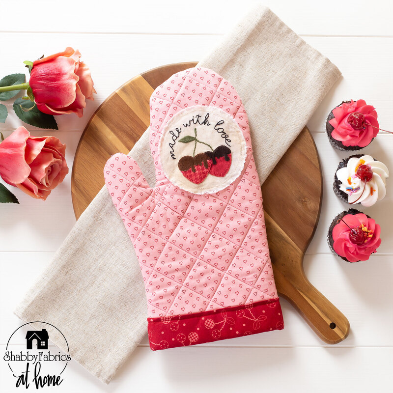 Photo of a pink oven mitt with red trim and a white circle depicting strawberries and the words 