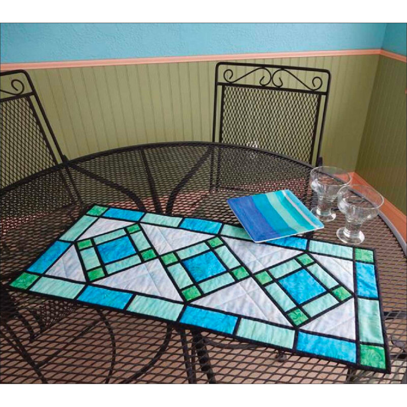 A geometric stained glass looking quilted table runner on a wire mesh table