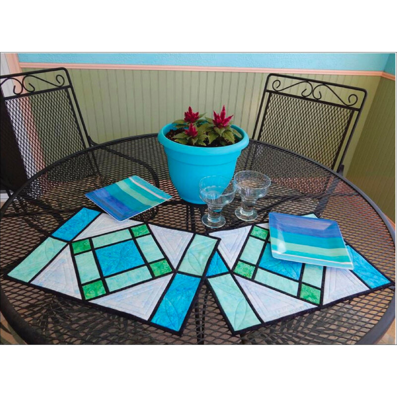 A pair of geometric stained glass looking quilted placemats on a wire mesh table