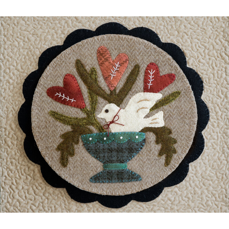 Image of a center circle mat for the Welcome Home wall hanging, featuring a dove splashing in a bird bath with heart shaped flowers behind it, crafted from wool 
