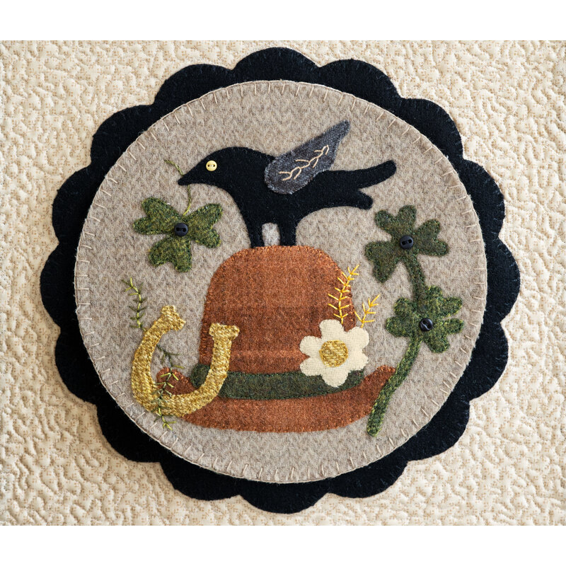 Image of a center circle mat for the Welcome Home wall hanging, featuring a crow on a leprechaun's hat with clovers and a horseshoe, crafted from wool 