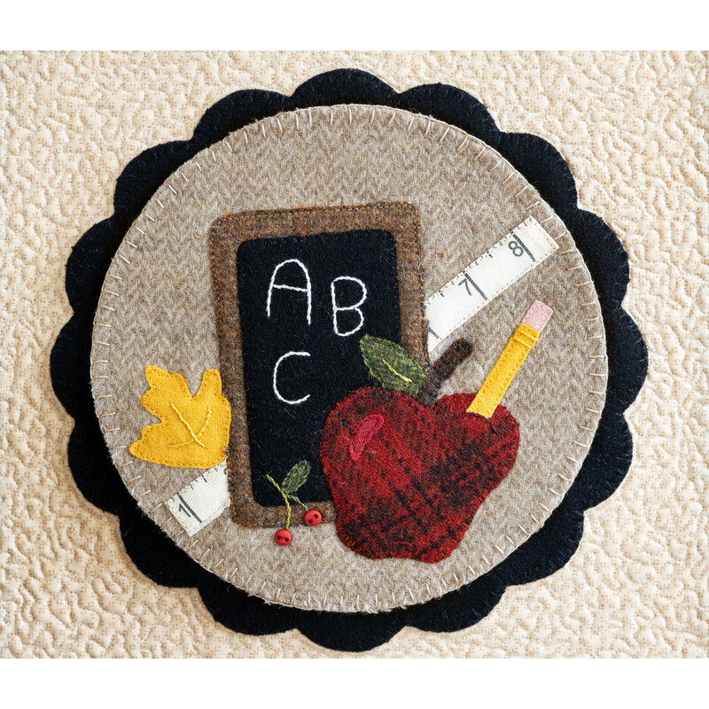 Image of a center circle mat for the Welcome Home wall hanging, featuring school supplies, an apple, and fall leaves crafted from wool 