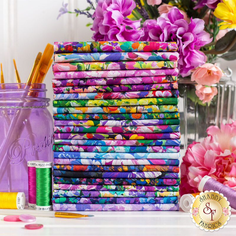 fabric with color painted florals stacked on a table next a purple jar full of paintbrushes