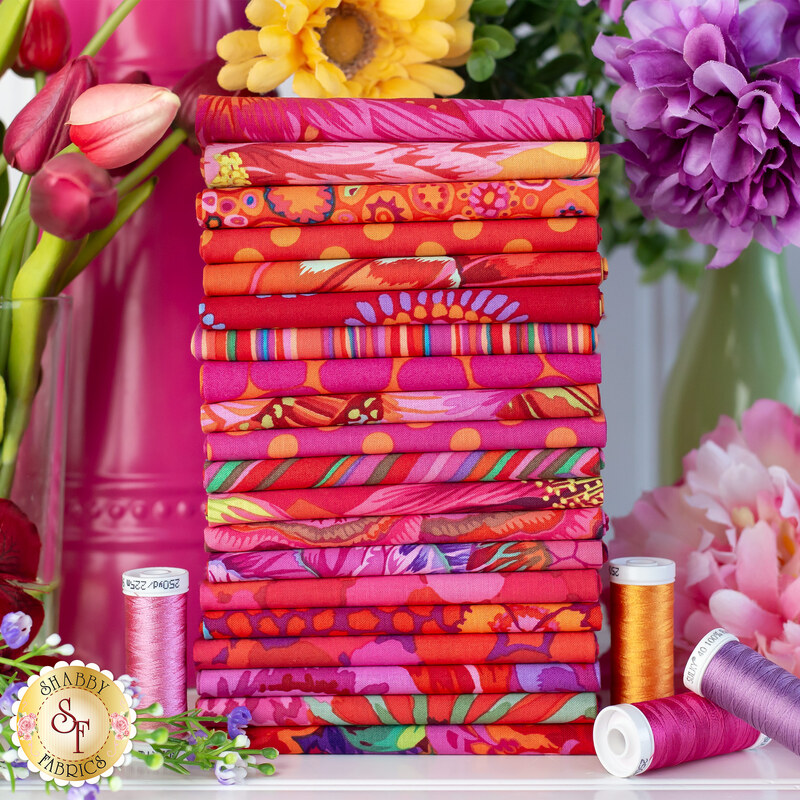  fabrics in shades of red, magenta, fuchsia, and orange stacked on a white table surrounded by flowers
